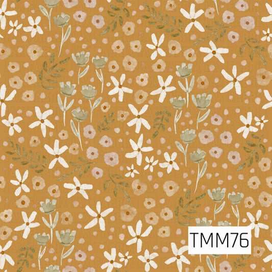 A warm watercolor floral pattern featuring creamy white daisies, soft sage green blooms, golden beige flowers, and dusty blush accents. Delicate olive leafy sprigs and scattered petals are arranged across a rich golden mustard background, creating a cozy, earthy botanical design with a soft vintage feel.
